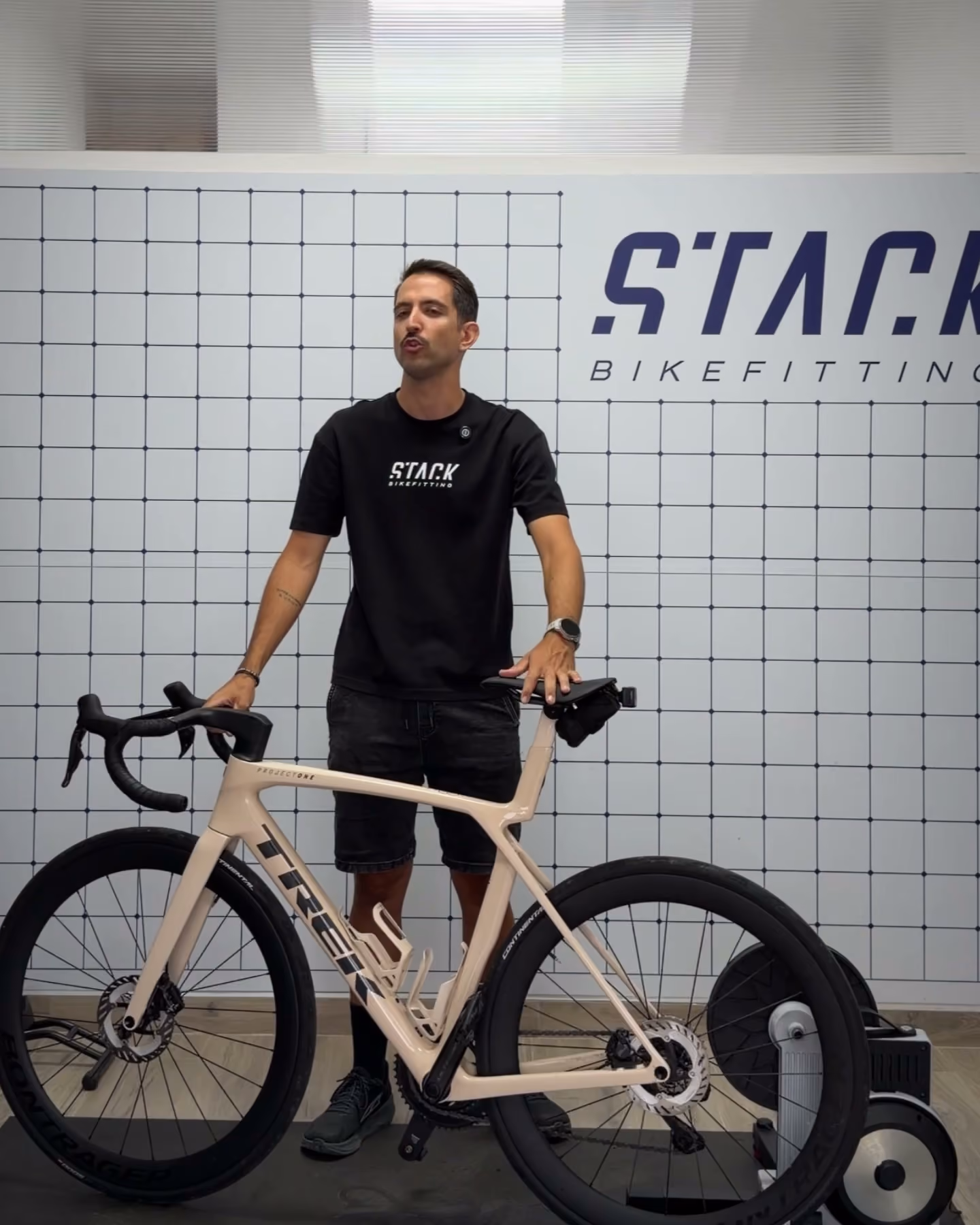Un técnico de Stack junto a una bicicleta de carretera montada sobre el rodillo, delante de la pared con el rótulo del estudio.